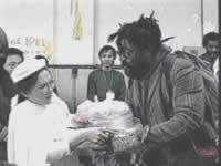 Foto da Suprema Mestra Ching Hai em uma ação caritativa junto a um homem em condições desfavoráveis.